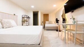 A modern hotel room with a large bed, a desk, a chair, a TV, and a bathroom. - Private terrace + panoramic view | Coworking (Medellín)