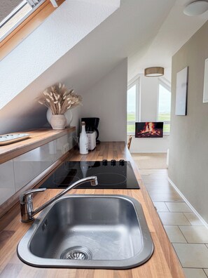 A modern kitchen with a built-in stove, a stainless steel sink, wooden countertops, a coffee maker, and a vase with dried plants. - Modern loft near the North Sea – quiet, stylish, and accommodating up to 4 guests (Dornum)