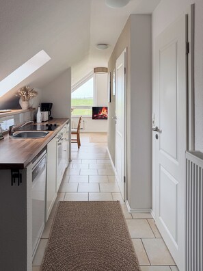 A modern kitchen with a built-in dishwasher, a coffee machine, and a TV displaying a fire. - Modern loft near the North Sea – quiet, stylish, and accommodating up to 4 guests (Dornum)