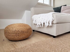 A room with a woven ottoman, a beige sofa with a white throw blanket, and a textured rug. - Modern loft near the North Sea – quiet, stylish, and accommodating up to 4 guests (Dornum)