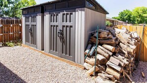 A wooden shed with two doors, a gravel ground, and a pile of firewood.