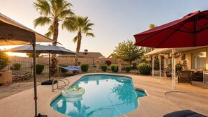 Ein Pool mit Liegestuhl und Sonnenschirm, umgeben von Palmen und einer Terrassenfläche.