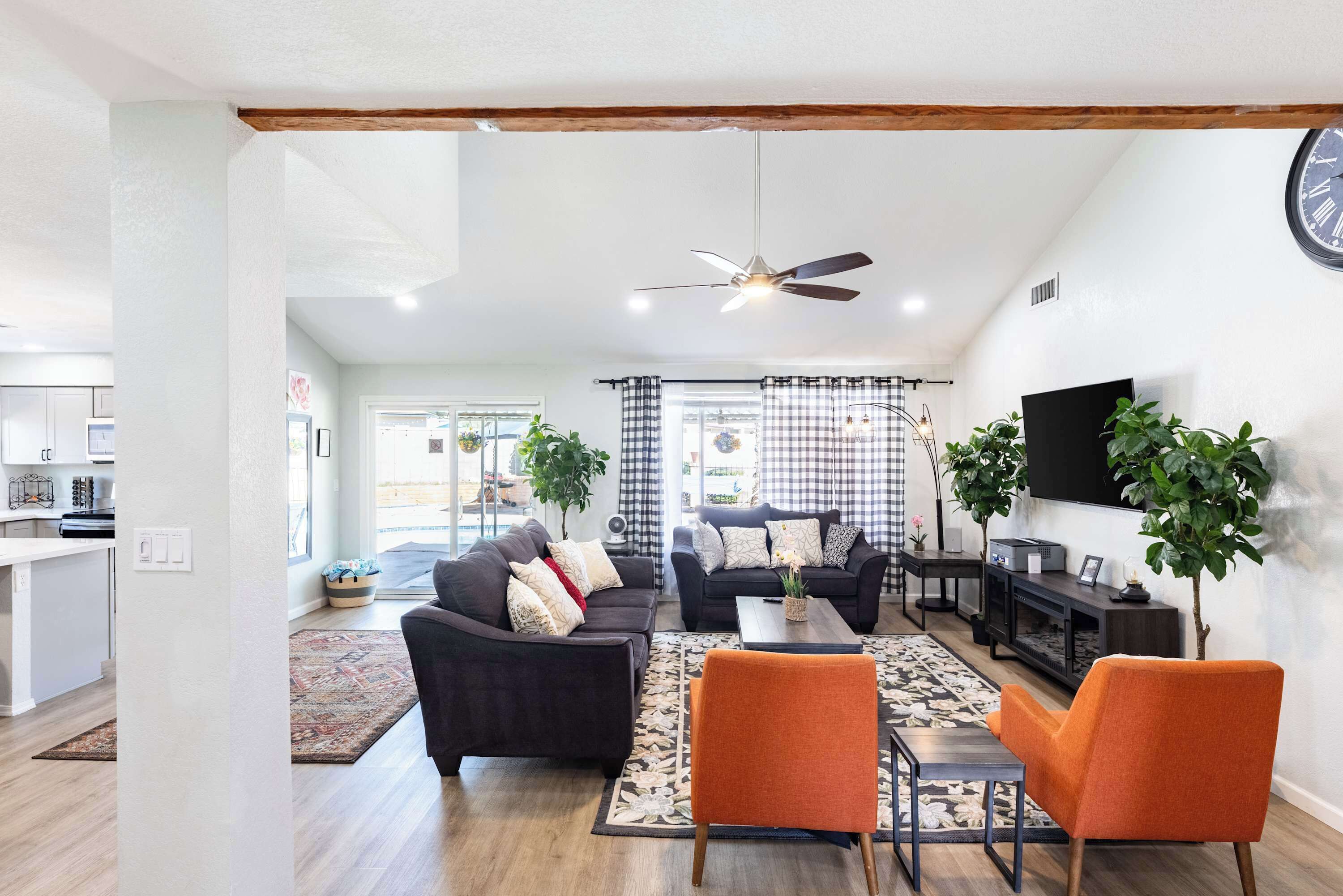 A living room with a sofa, armchairs, a coffee table, and a TV. There is a ceiling fan, a clock, and a plant.