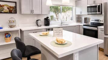 A modern kitchen with white cabinetry, a central island, a microwave, an oven, and a coffee maker.