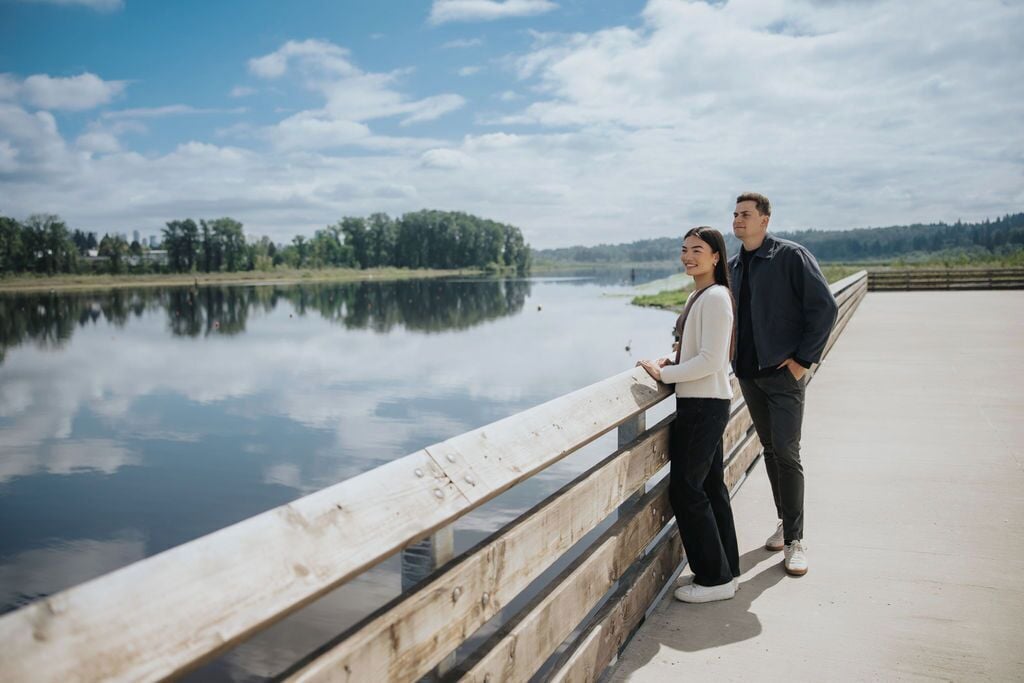 Pariskunta seisoo sillalla, taustalla on tyyni järvi ja puita.