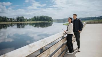 A couple standing on a bridge with a calm lake and trees in the background.