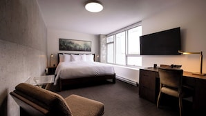 A hotel room with a bed, a desk, a chair, a TV, and a window. - Hotel Burnaby (Burnaby)