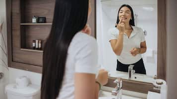 A bathroom with a mirror, sink, and toiletries on shelves.