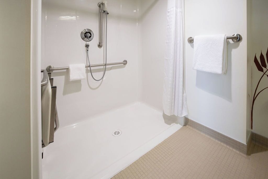 A bathroom with a walk-in shower, grab bars, a towel rack, and a toilet.