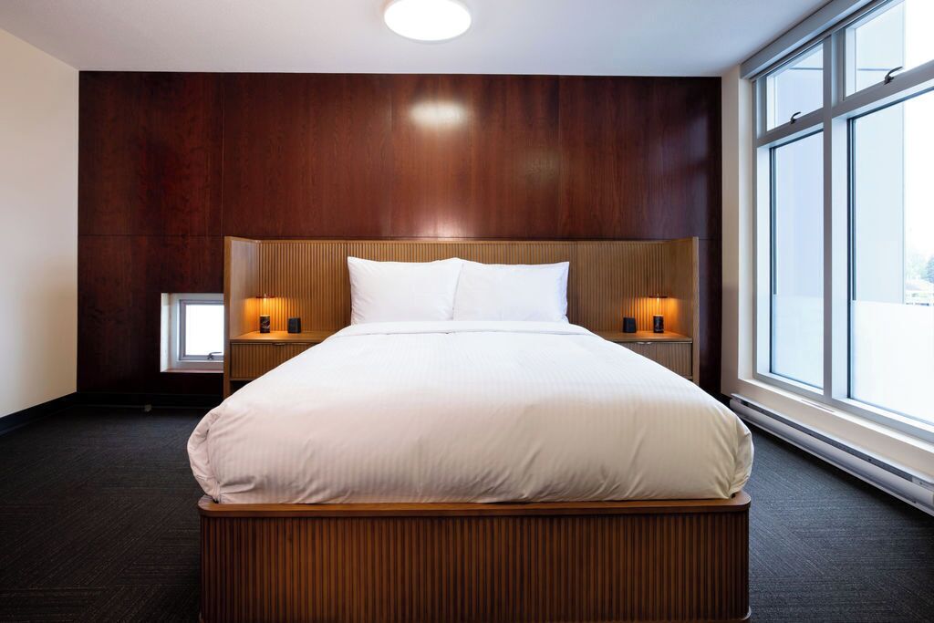 A hotel room with a large bed, wooden headboard, two bedside tables with lamps, and a large window.