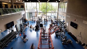 A multi-level gym with various exercise equipment, a blue floor, and large windows. - Hotel Burnaby (Burnaby)