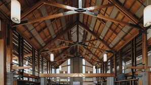 A large hall with high ceilings and wooden beams, furnished with tables and chairs, and a television screen mounted on the wall. - Hotel Burnaby (Burnaby)