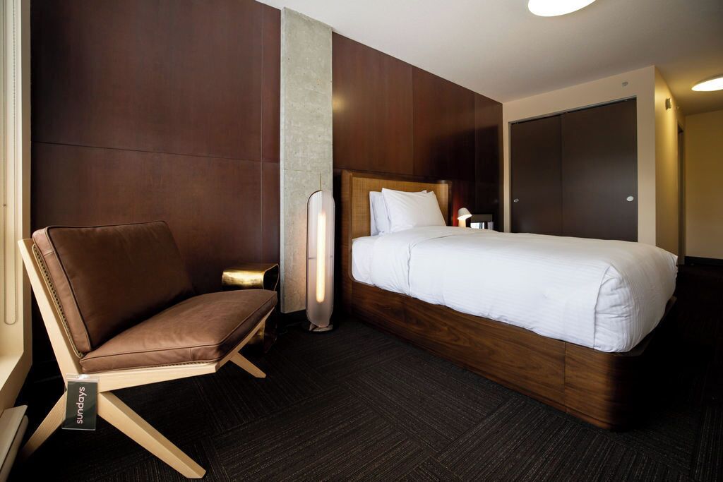 A hotel room with a bed, a chair, a bedside table, and a wardrobe.