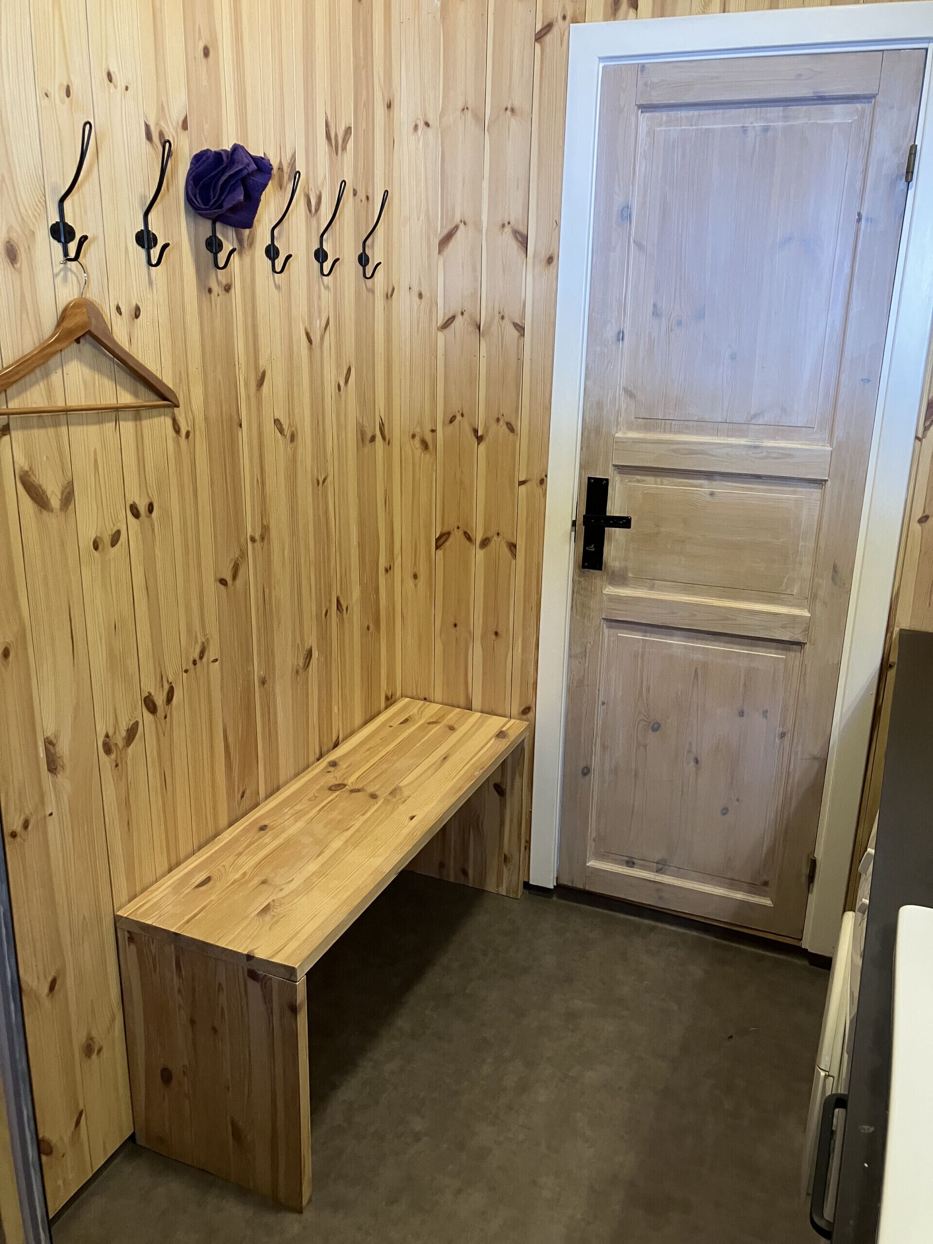 Un banc en bois, une porte et des crochets fixés au mur, avec un tissu violet.