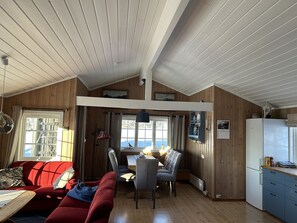 Interior acollidor d'una cabana amb zona de menjador, sofà, taula i nevera.
