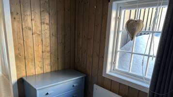 A room with wooden walls, a window with a heart-shaped decoration, a radiator, and a blue dresser.