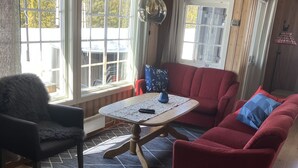 A cozy living room with a wooden floor, a red sofa, a black chair, and a table with a remote control. - Mountain cabin in Lillehammer (Lillehammer)