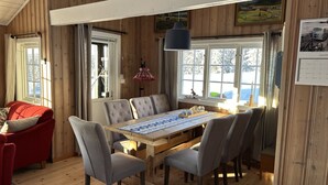 A wooden interior with a dining table, chairs, a red sofa, and a window with a view of snow-covered trees. - Mountain cabin in Lillehammer (Lillehammer)