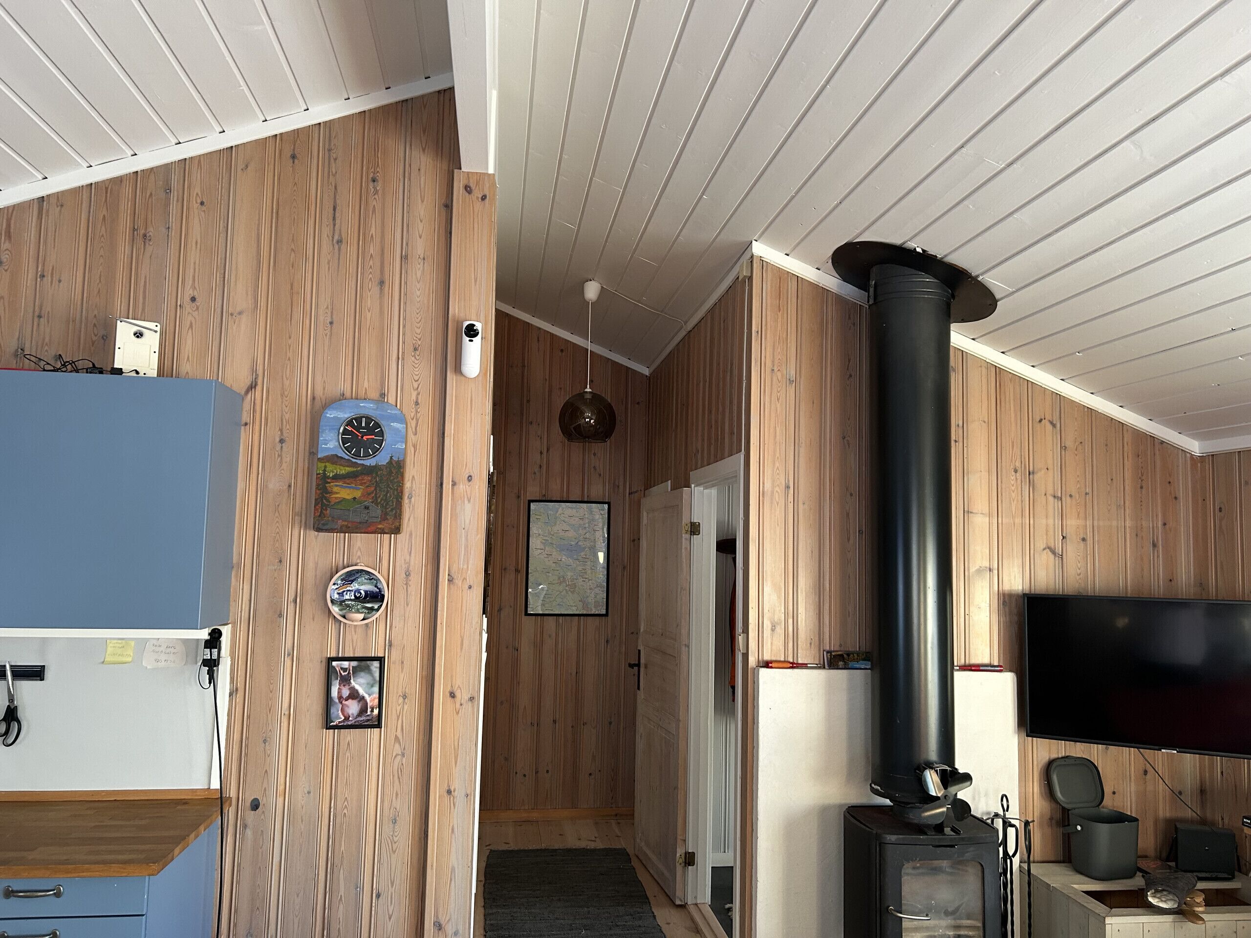 Ein Zimmer mit Holzwandverkleidung, einem schwarzen Herd, einem Fernseher und einer Tür zu einem anderen Raum.