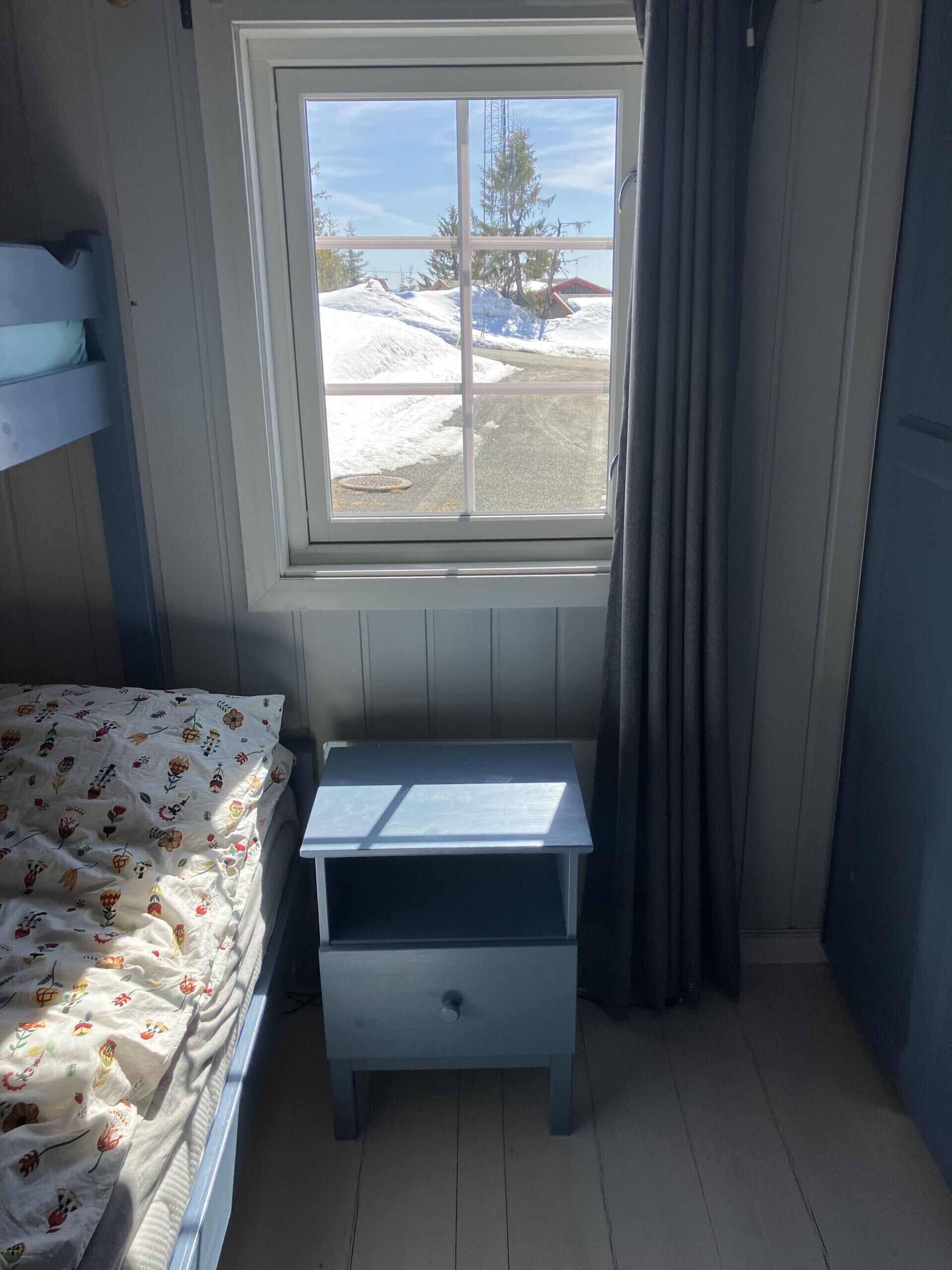 A room with a bunk bed, a small table, a window with curtains, and a view of a snowy landscape.