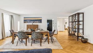 Ein Essbereich mit einem Holztisch, gedeckt für vier Personen, einem Stadtbildgemälde darüber und einer großen Kommode im Hintergrund.