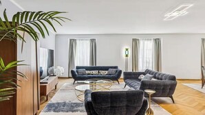 Ein modernes Wohnzimmer mit einer Couch, Sesseln, einem Couchtisch und einem Fernseher.