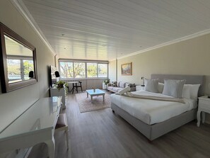 Een slaapkamer met een bed, nachtkastjes, een bureau en een stoel. Er zijn ramen die zorgen voor natuurlijk licht.