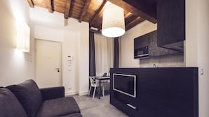 A modern living space with a dark sofa, a dining area, and a kitchen with a TV. - Dolcevita Panisperna 6 Gina Loft Apartment (Rome)