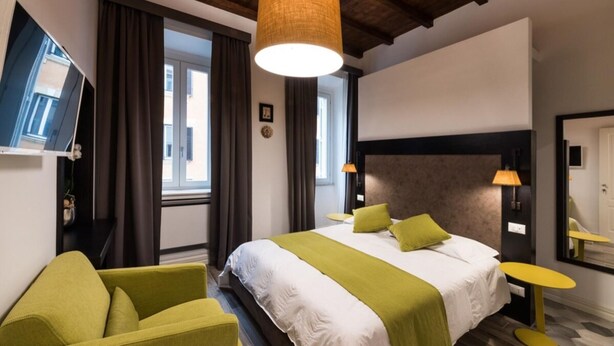 A hotel room with a bed, a television, a window with curtains, a wooden ceiling, and a yellow side table. - Dolcevita Panisperna 1 Norma Apartment (Rome)