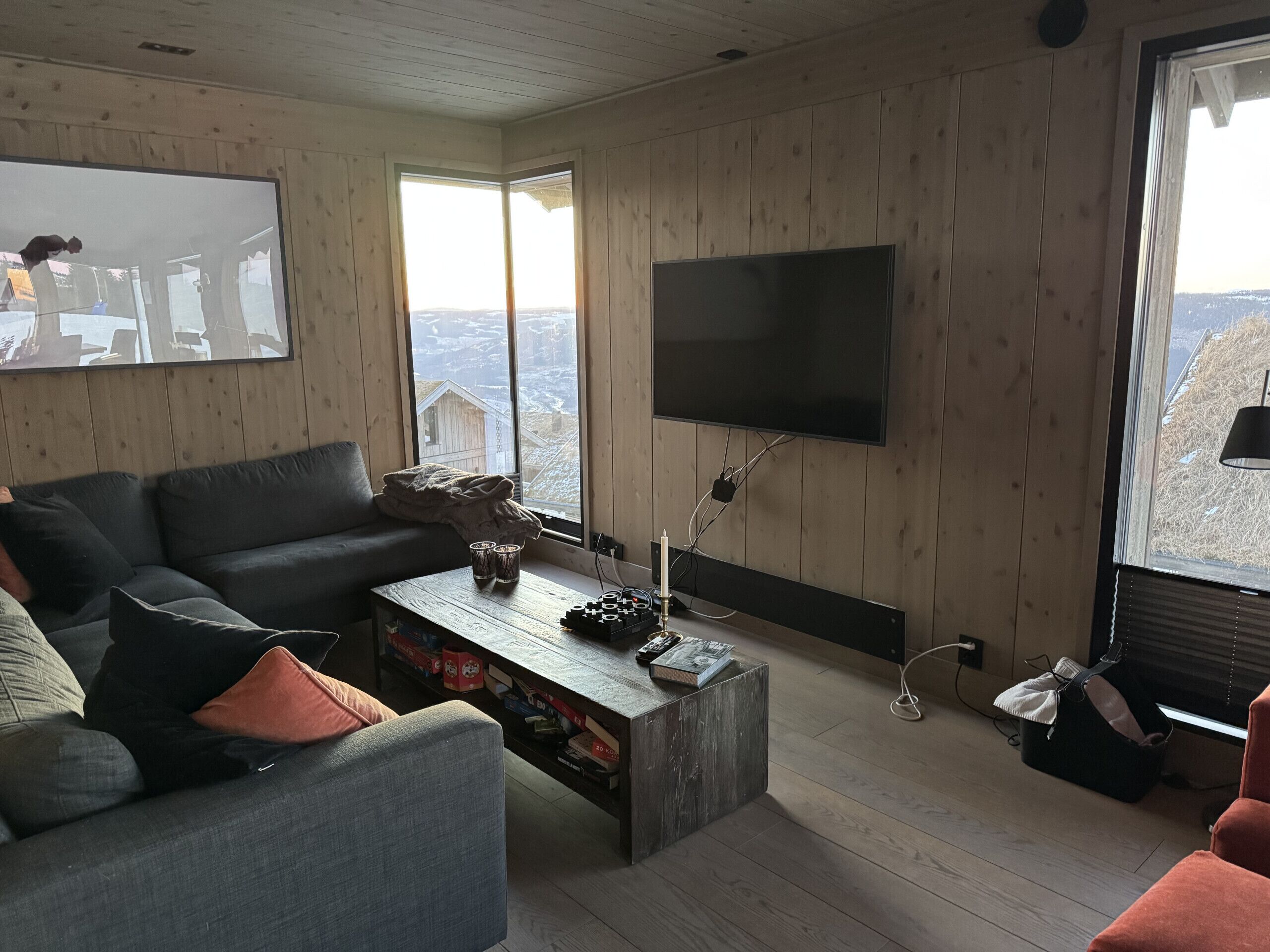 A living room with a large flat-screen TV mounted on the wall, a wooden coffee table, a sofa, and a window with a view of a snowy landscape.