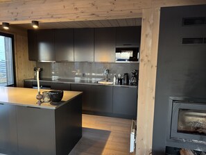 Une cuisine moderne avec des meubles de couleur sombre, un îlot central en bois et un poêle à bois.