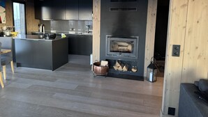A modern kitchen with a central island, a built-in wood stove, and a dining area with a wooden ceiling.