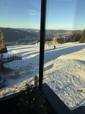 A snowy mountain slope with a ski lift, a wooden cabin, and a clear view of the surrounding landscape.