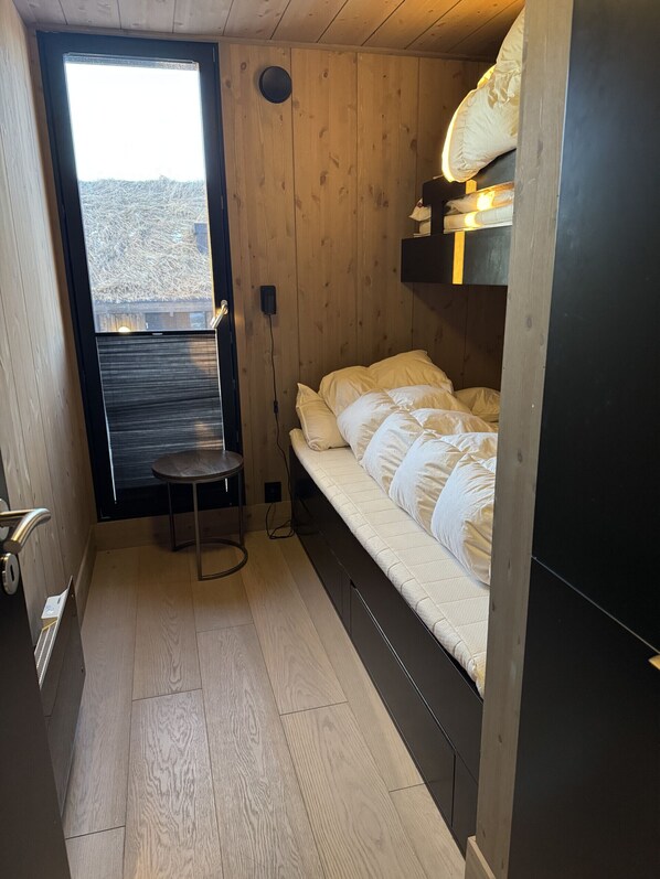 A compact room with a bed, a small table, and a window with a view of a wooden structure outside.