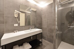 Ein modernes Badezimmer mit einem großen Waschbecken, einem Spiegel, einem Föhn und einer Duschkabine.