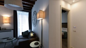 A modern room with a sofa, a small table, a lamp, and a clock on the wall. - Dolcevita Panisperna 5 Audrey Ground Floor Apartment (Rome)
