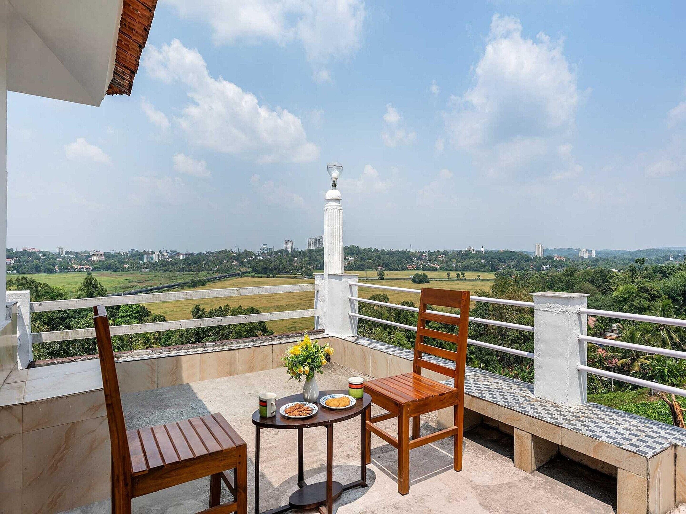 Een balkon met een tafel, stoelen en een bloevas.