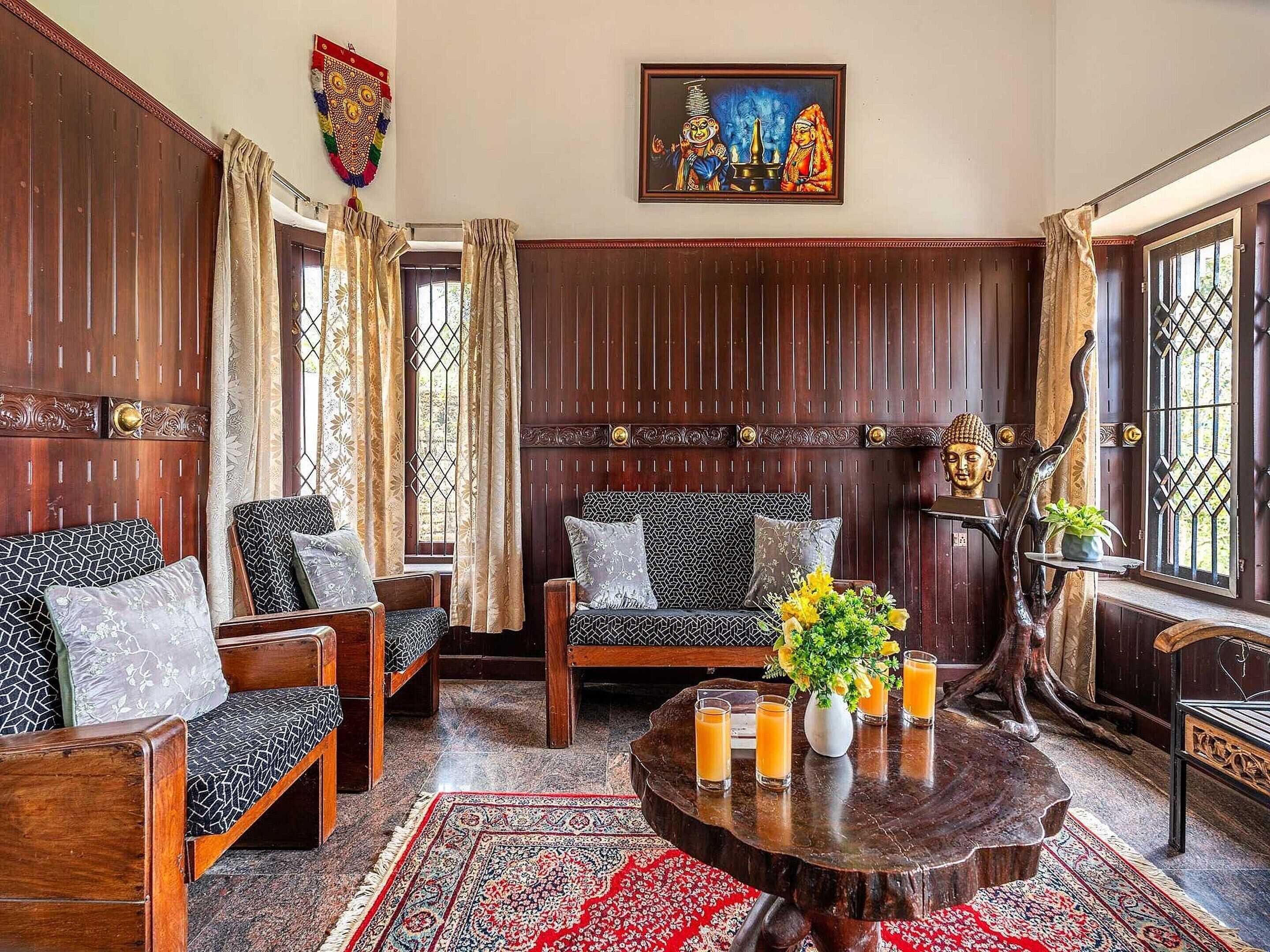 Una habitación tradicional con paneles de madera, sofás estampados, una mesa de centro redonda de madera con bebidas y una estatua de Buda.