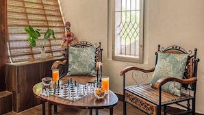 Una habitación con un tablero de ajedrez, dos sillas, una mesa, un ventanal con rejas de metal y una planta.