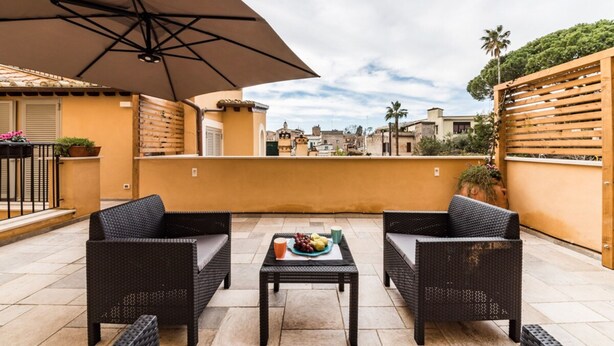 A terrace with wicker furniture, a table with fruit, and a view of the city. - Dolcevita Panisperna 4 - Liz Apartment (Rome)