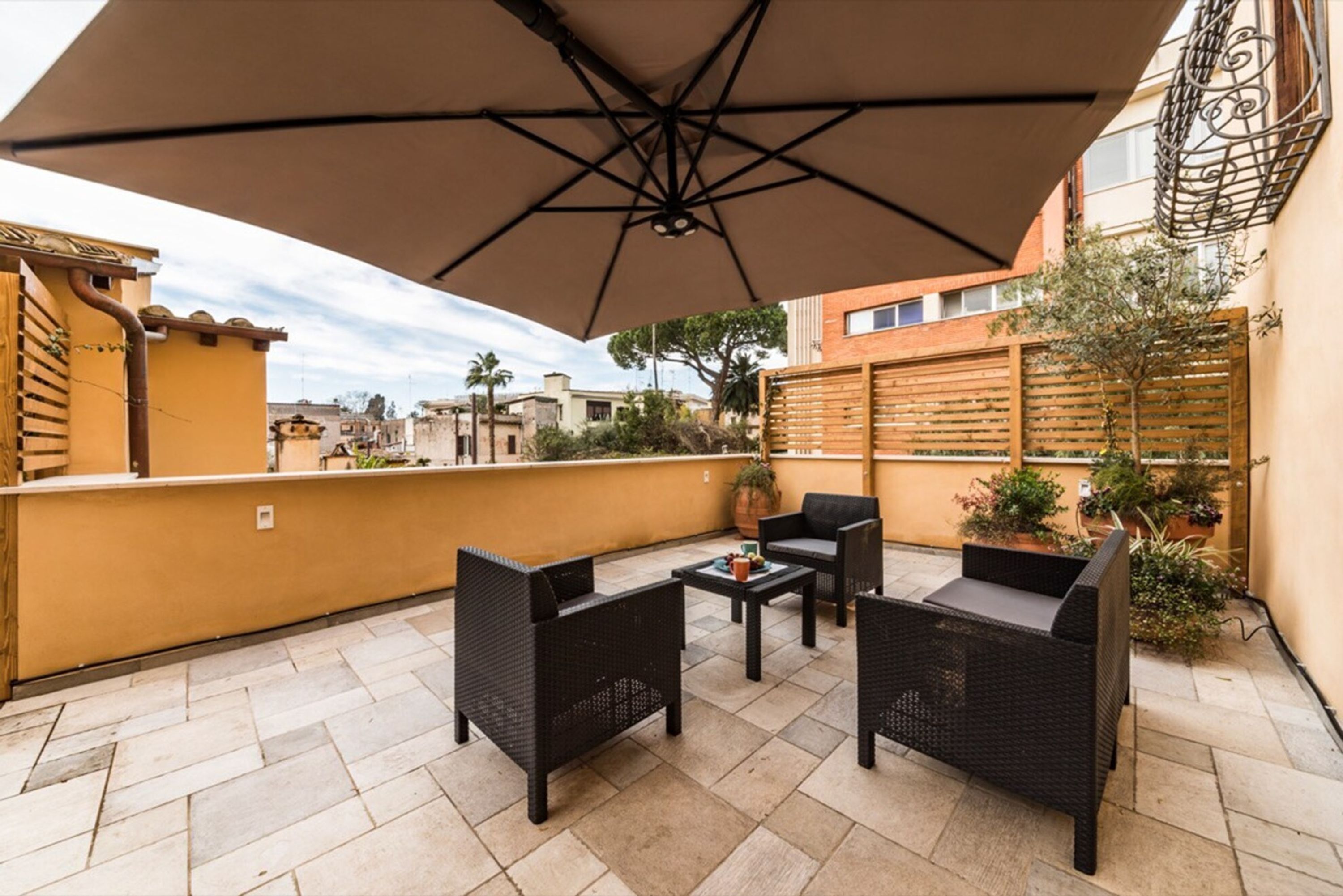Eine Terrasse im Freien mit Korbmöbeln, einem großen Sonnenschirm und Topfpflanzen.