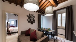 A modern living room with a sofa, a dining table with chairs, a large window, and a ceiling with exposed beams. - Dolcevita Panisperna 4 - Liz Apartment (Rome)