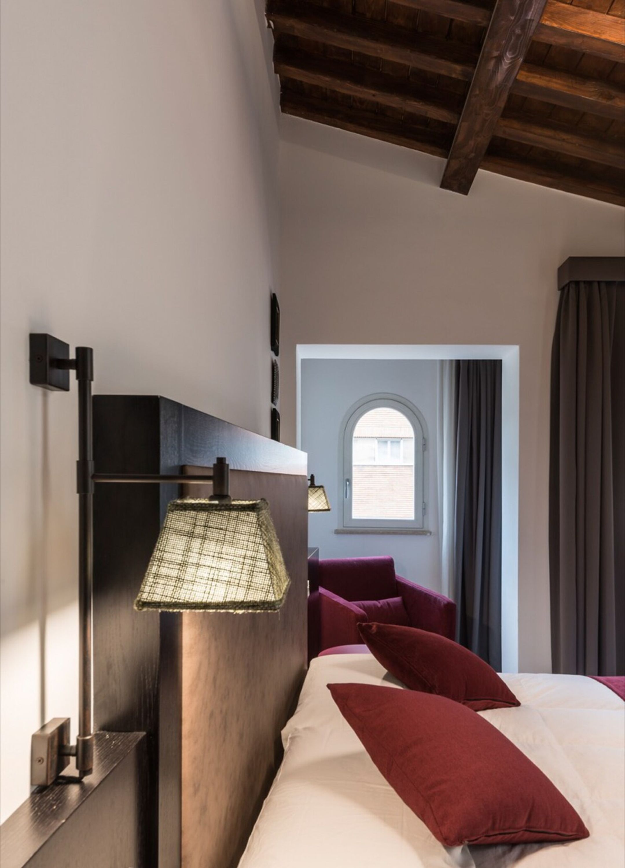 Un dormitorio con cama, lámpara de pared, ventana con cortinas y vistas al exterior.