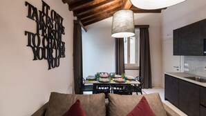 A dining area with a table set for four, a kitchen with dark cabinets, and a ceiling with exposed wooden beams. - Dolcevita Panisperna 4 - Liz Apartment (Rome)