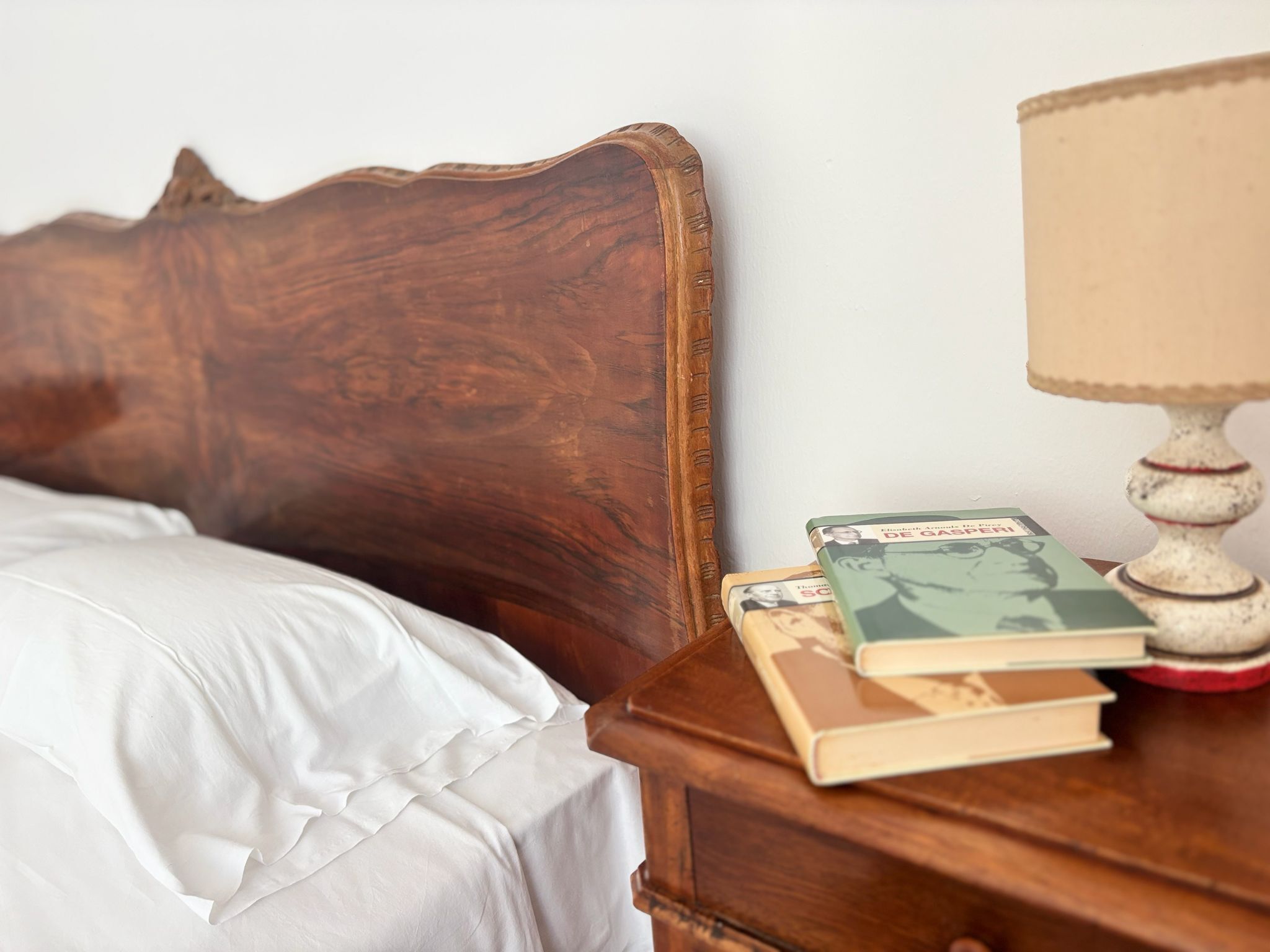 A wooden headboard, a white pillow, a bedside table with books and a lamp.