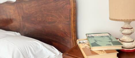 A wooden headboard, a white pillow, a bedside table with books and a lamp.