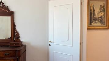 Een witte, gesloten deur met een eenvoudig ontwerp, een houten dressoir met laden aan de linkerkant en een lijst met schilderij aan de rechterkant.