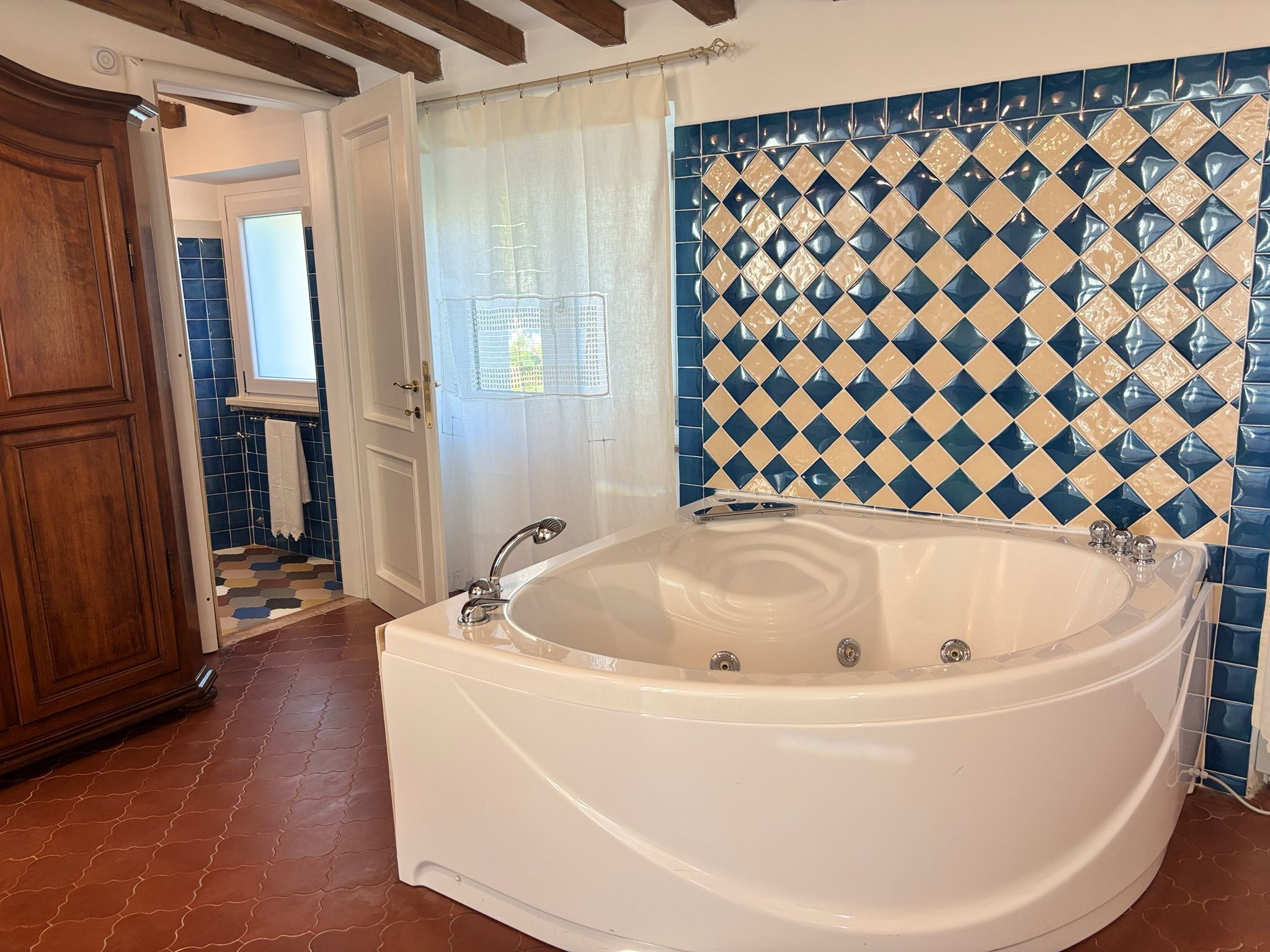 A bathroom with a freestanding bathtub, a wooden door, and blue and beige patterned tiles.