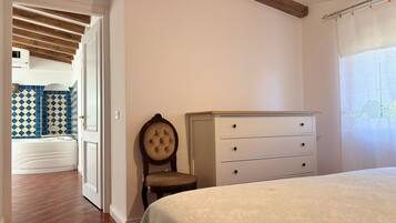 Un dormitorio con cama, cómoda, silla y vistas a un baño con baldosas estampadas.