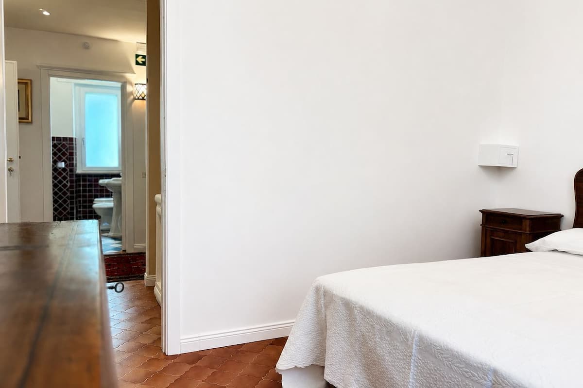 A bedroom with a bed, a nightstand, a wooden dresser, and a bathroom visible through an open door.